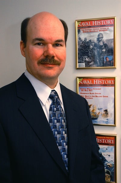 Portrait of Mr. Richard Latture in his office standing by framed covers of Naval History Magazine.