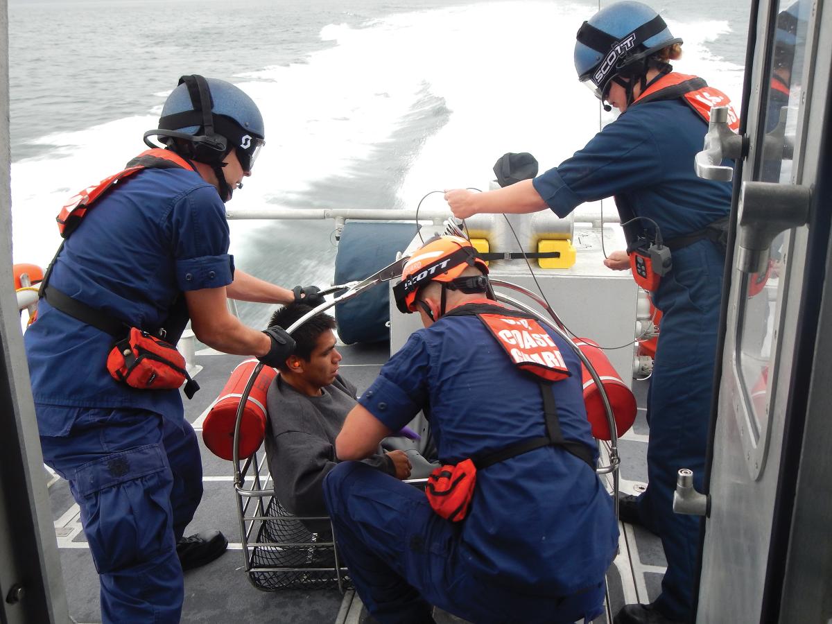 A boat crew from Coast Guard Station Bellingham, Washington, prepares an injured diver to be hoisted from the deck of a 45-foot response boat—medium into an MH-65 Dolphin helicopter after he suffered a diving accident near Patos Island.