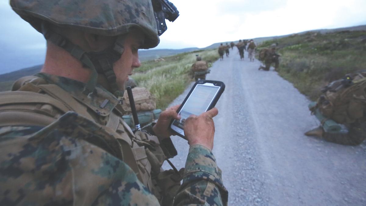 Marine holding a handheld mobile device on a road in an operating environment